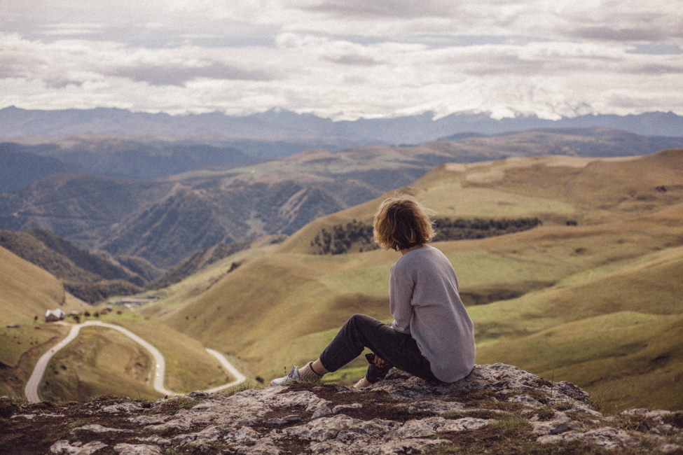 kobieta siedząca na szczycie góry patrząca na zielone góry i doliny
