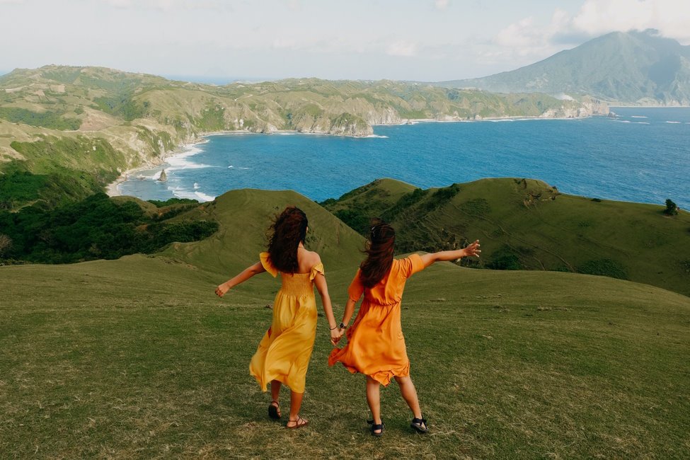 dwie-kobiety-w-zoltej-i-pomaranczowej-sukience-stojace-na-wzgorzu-z-widokiem-na-morze