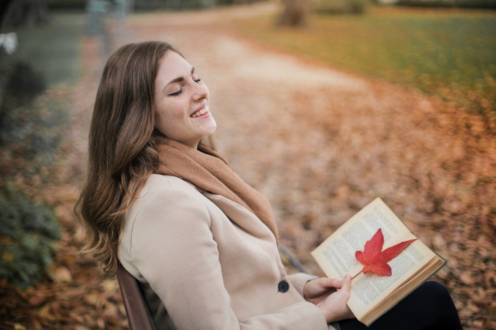 usmiechnieta-kobieta-na-lawce-w-parku-jesienia-czyta-ksiazke